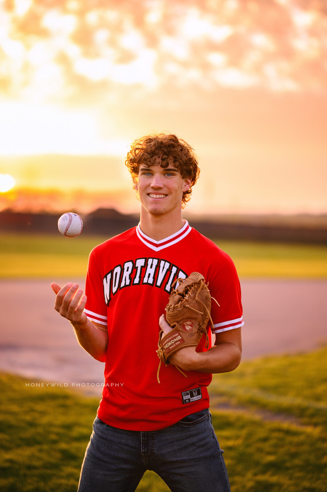 grand rapids senior boy at sunset smiling while throwing a baseball