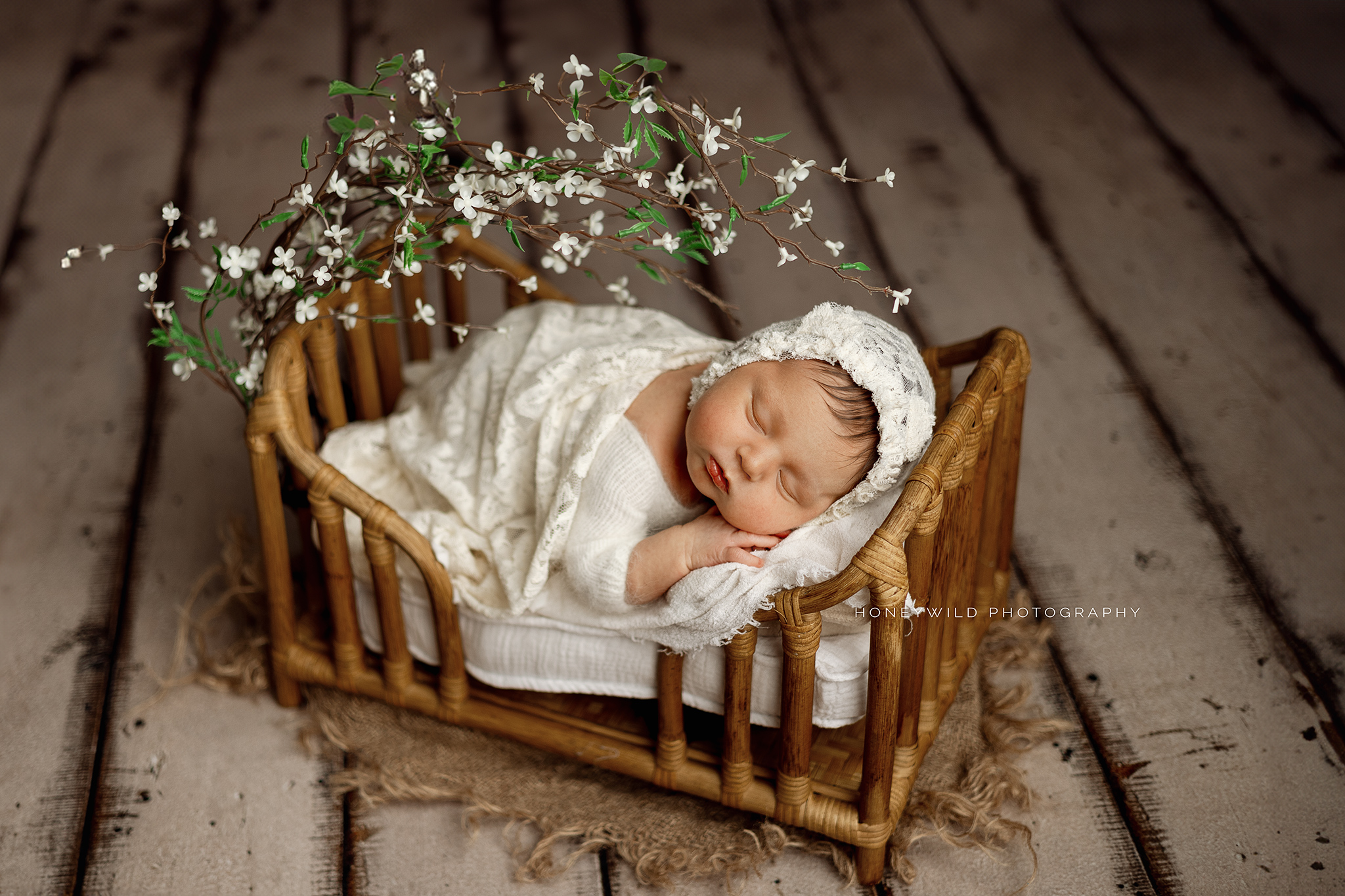 (direct upload)
A newborn baby dressed in white sleeps peacefully in a small, rustic wooden bed adorned with delicate white flowers. The baby is wrapped in a white blanket and wears a matching bonnet. The background features a wooden floor, creating a cozy and serene atmosphere captured by a Grand Rapids newborn photographer.