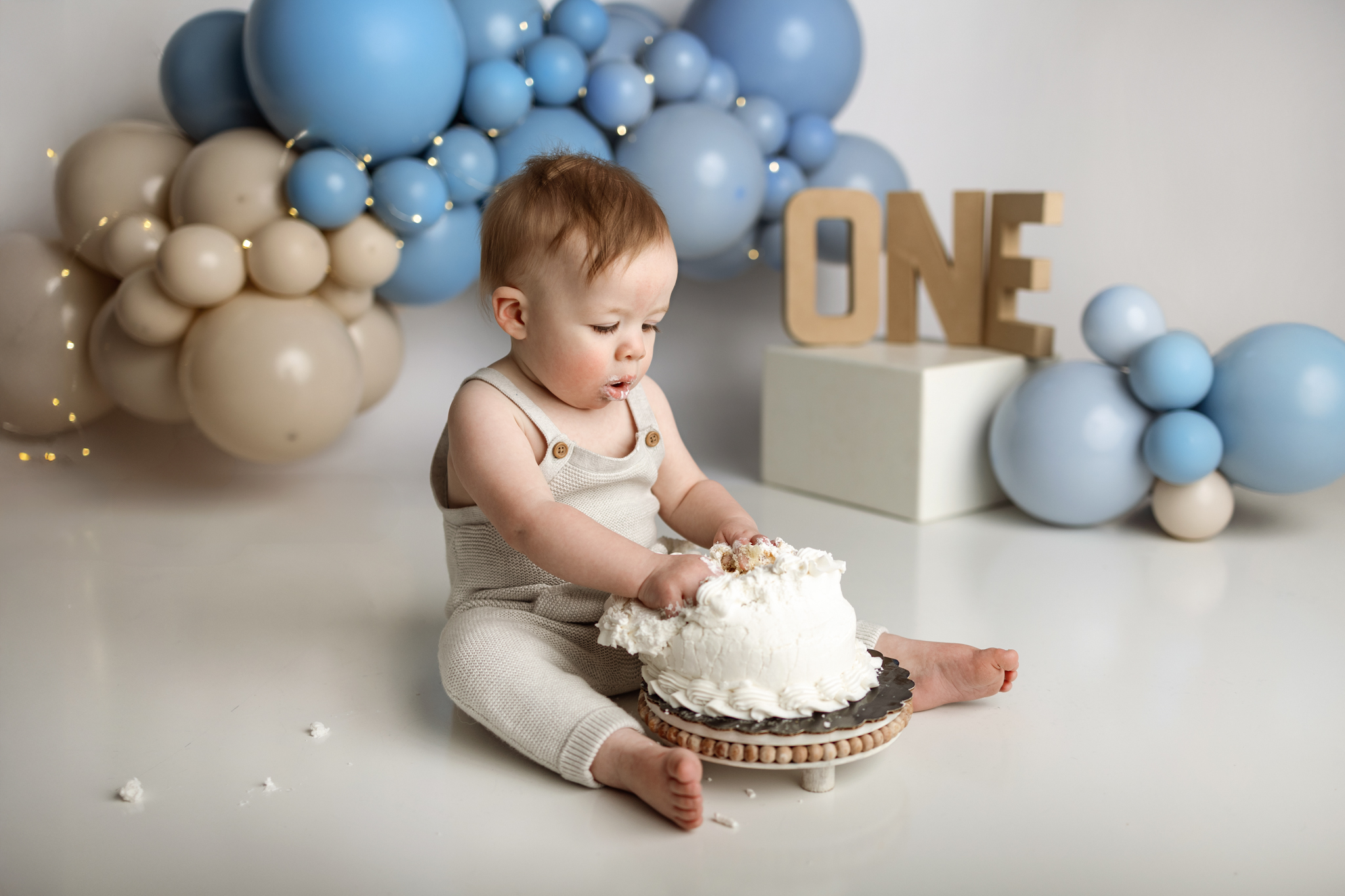 Baby boy digging into a white cake with frosting-covered hands during a one-year photo session in Grand Rapids, Michigan