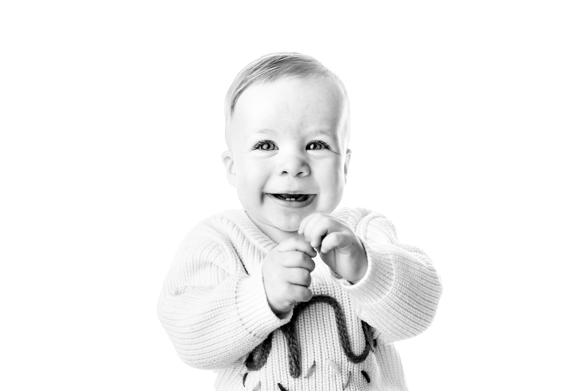 Black-and-white close-up of a smiling one-year-old baby wearing a 'one' sweater during a milestone session in Grand Rapids, Michigan