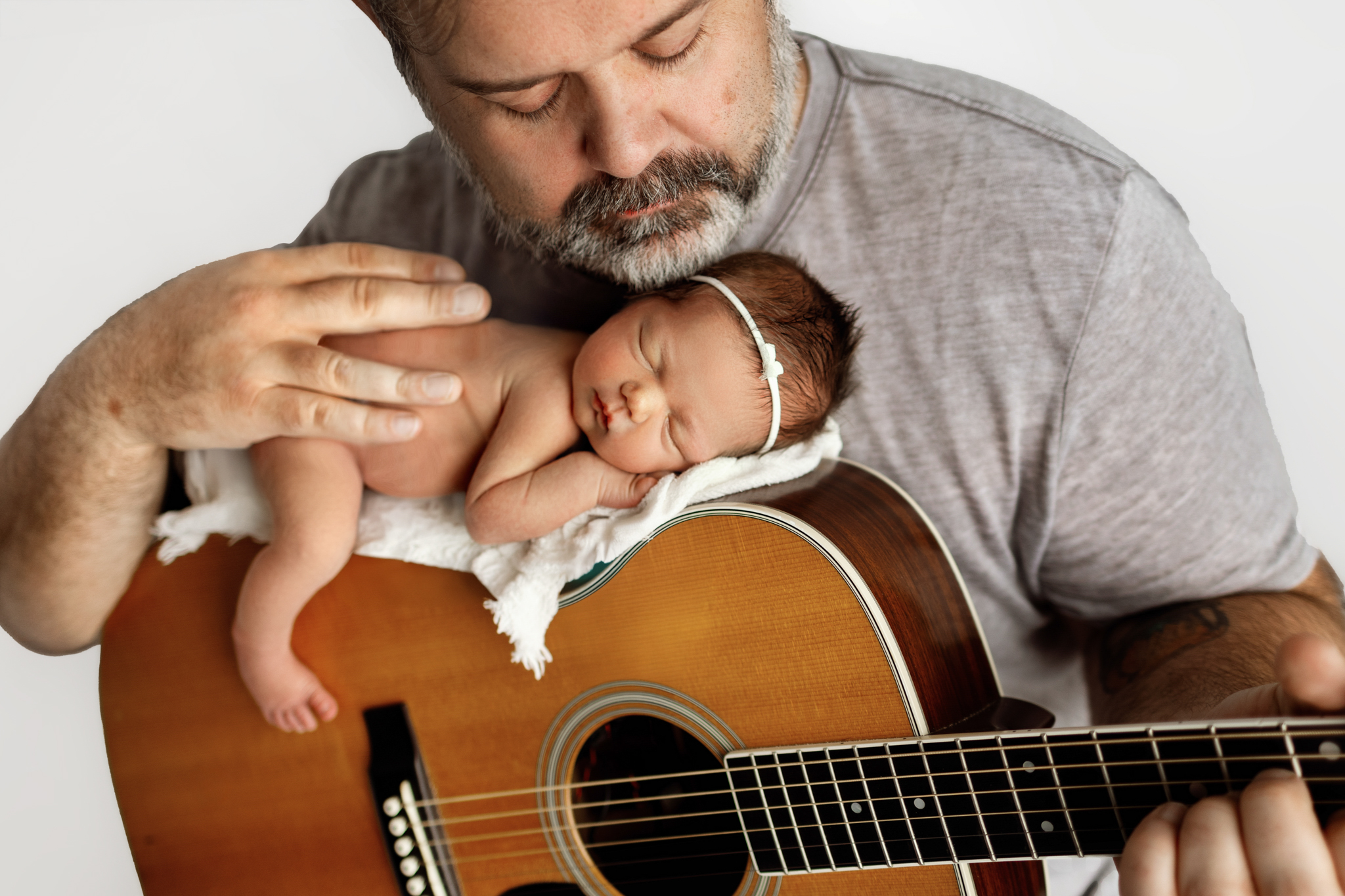 Father gently cradling his newborn daughter on his guitar during a Honey Wild Photography session in Grand Rapids, Michigan