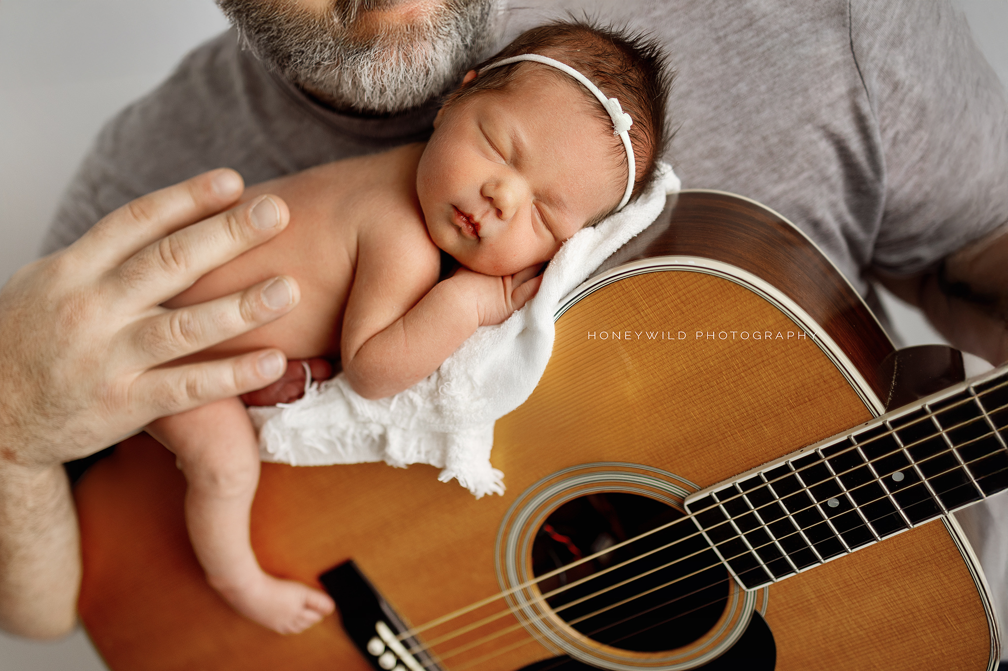 Newborn baby girl peacefully resting on a guitar, showcasing a meaningful and personal prop in a Grand Rapids photography session