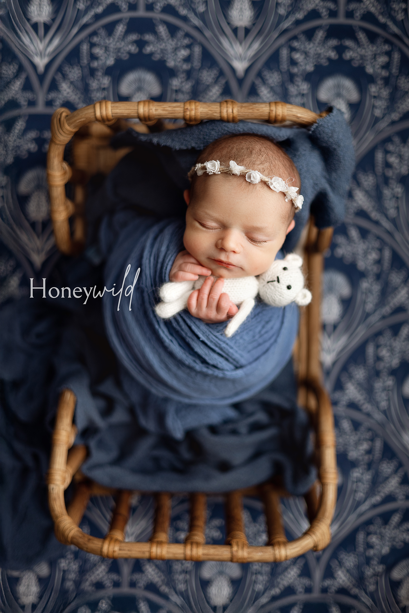 Newborn baby wrapped in deep blue swaddle, holding a tiny teddy bear – artistic newborn photography session in Grand Rapids, MI