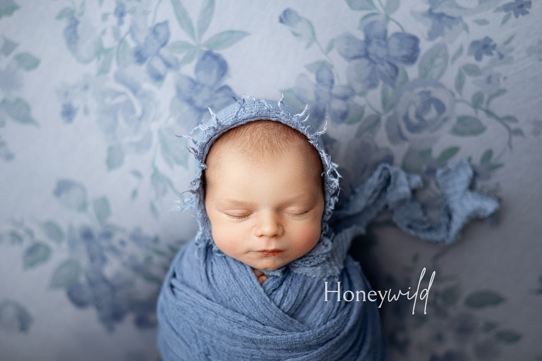 Close-up of newborn baby girl wrapped in textured blue bonnet and swaddle, sleeping peacefully – fine art newborn photography Grand Rapids