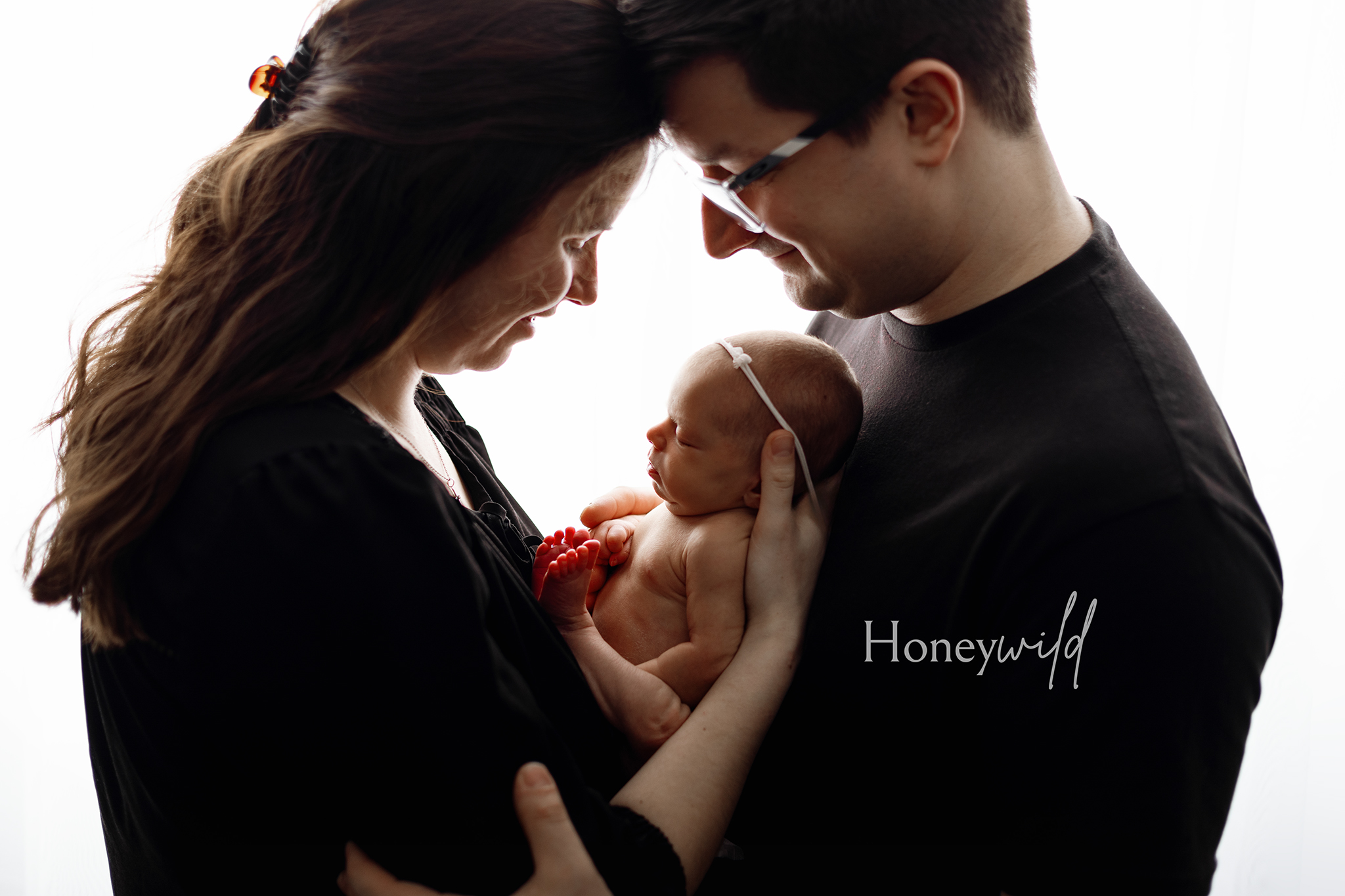 Parents holding newborn baby together, silhouetted against a bright window – emotional and intimate newborn family photography in Grand Rapids.