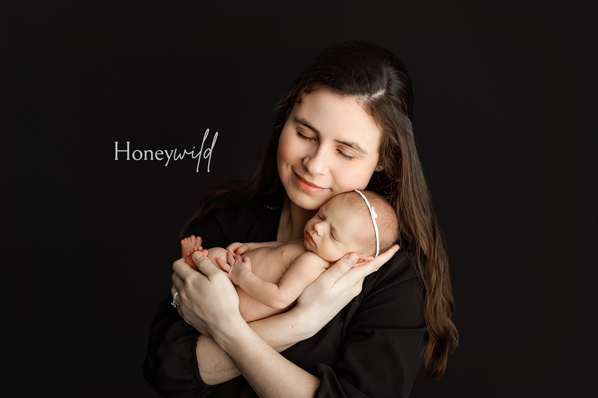 Mother embracing newborn baby against a dark backdrop, eyes closed – warm and intimate newborn photography in Grand Rapids.