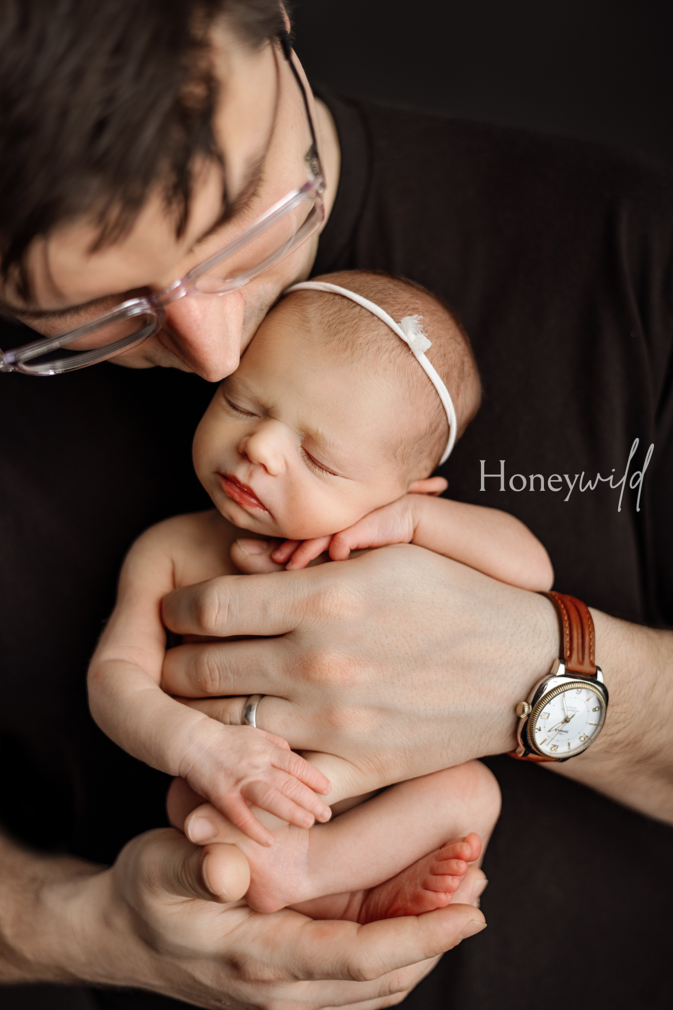 Father holding newborn baby girl in hands, kissing her head – cozy newborn photography session in Grand Rapids studio