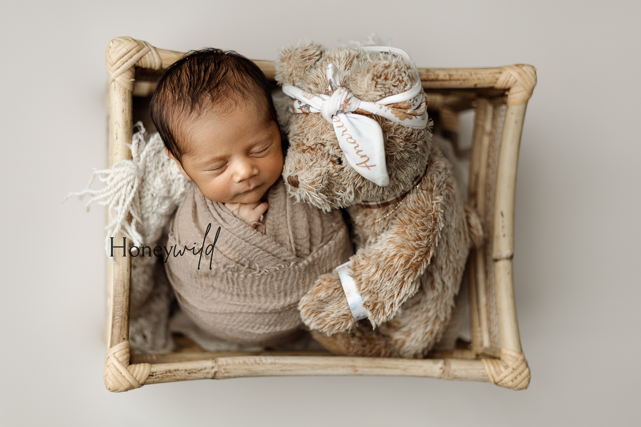 Newborn wrapped in neutral tones snuggled with a teddy bear inside a small basket during a Honeywild Photography session, featuring natural newborn photography in Grand Rapids, Michigan