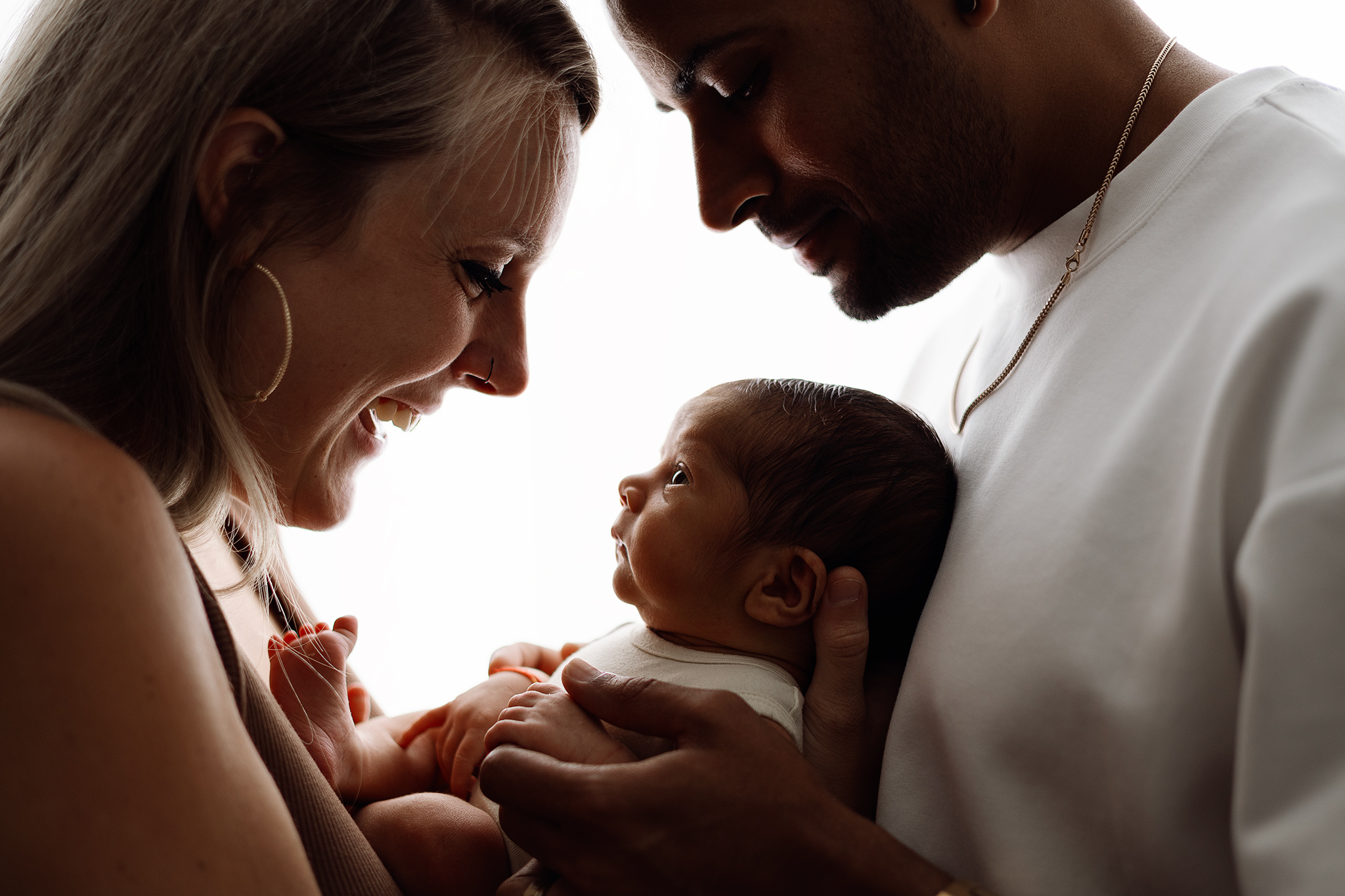 Backlit family moment with parents holding their newborn baby, photographed by Honeywild Photography, specializing in newborn photography in Grand Rapids, MI.