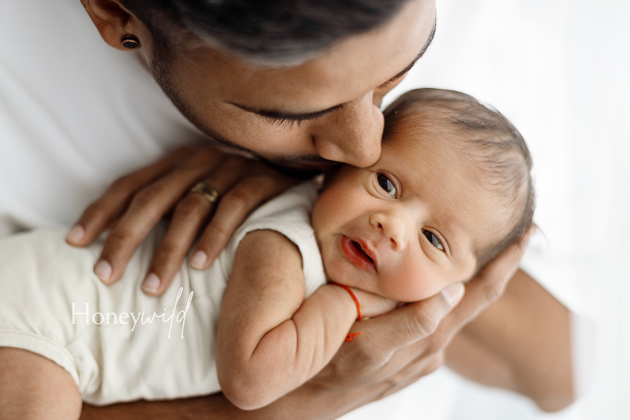 Father kissing his newborn’s head while holding them close during a Honeywild Photography session, highlighting lifestyle newborn photography in Grand Rapids, MI