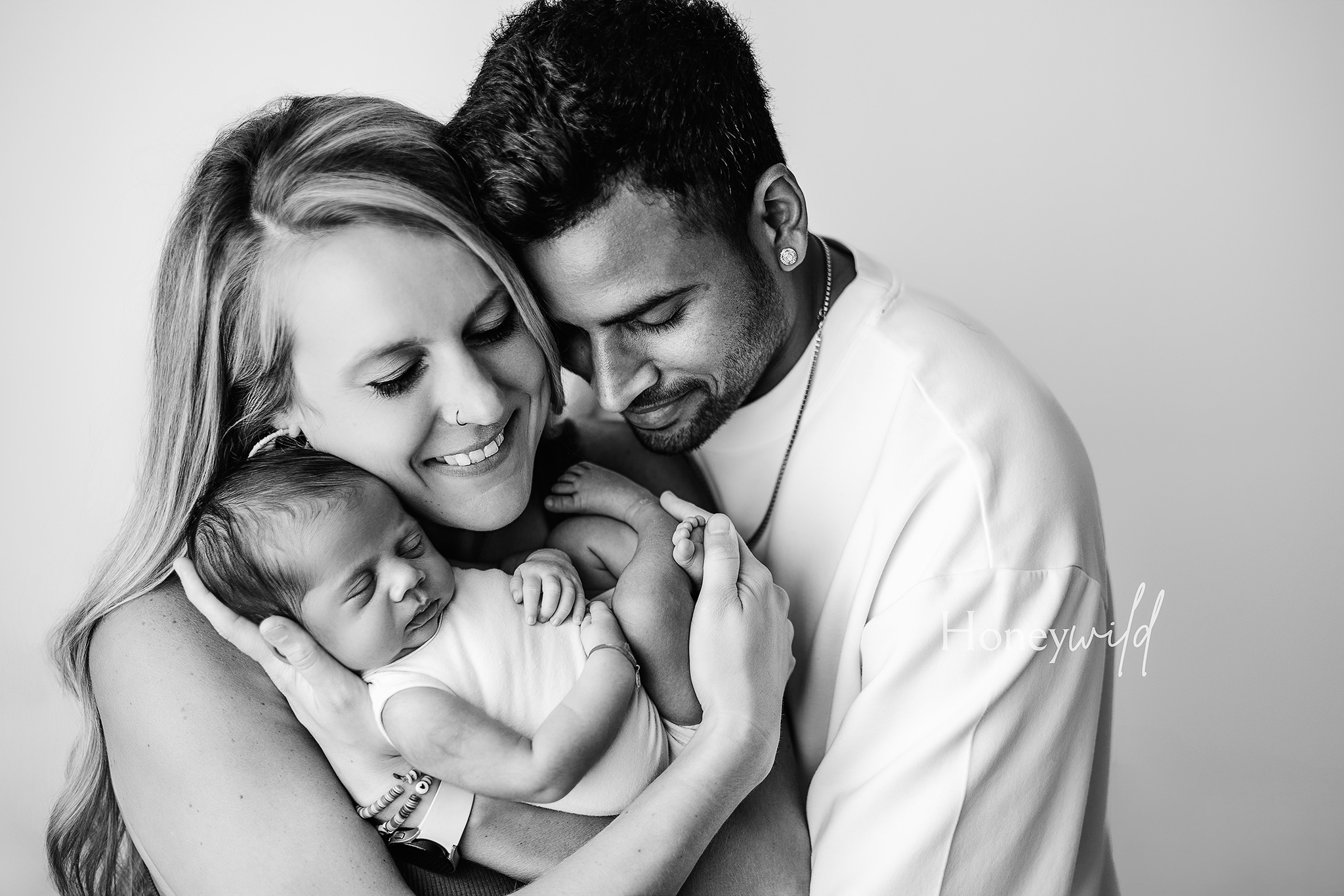 Black and white family portrait of new parents holding their newborn close, captured by Honeywild Photography specializing in newborn photography in Grand Rapids, Michigan