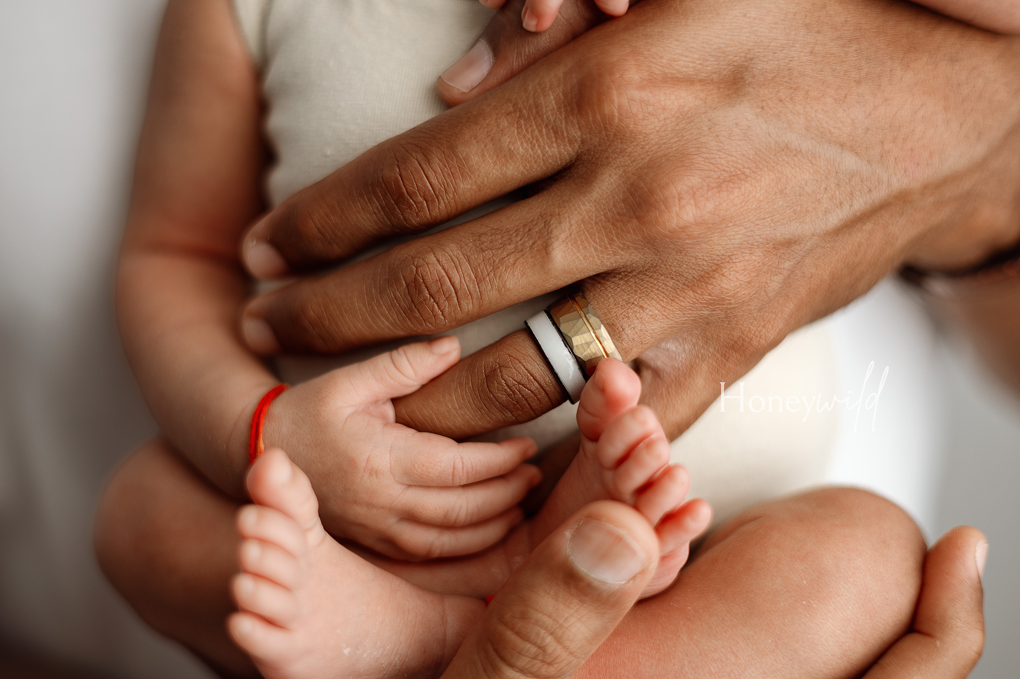 “Close-up detail of a newborn’s tiny hands and feet being held by their father during a Honeywild Photography session, showcasing natural newborn photography in Grand Rapids, Michigan.”