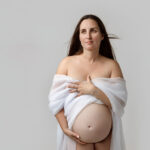 Minimal studio maternity photography of a pregnant mother standing confidently against a neutral backdrop in a Grand Rapids studio
