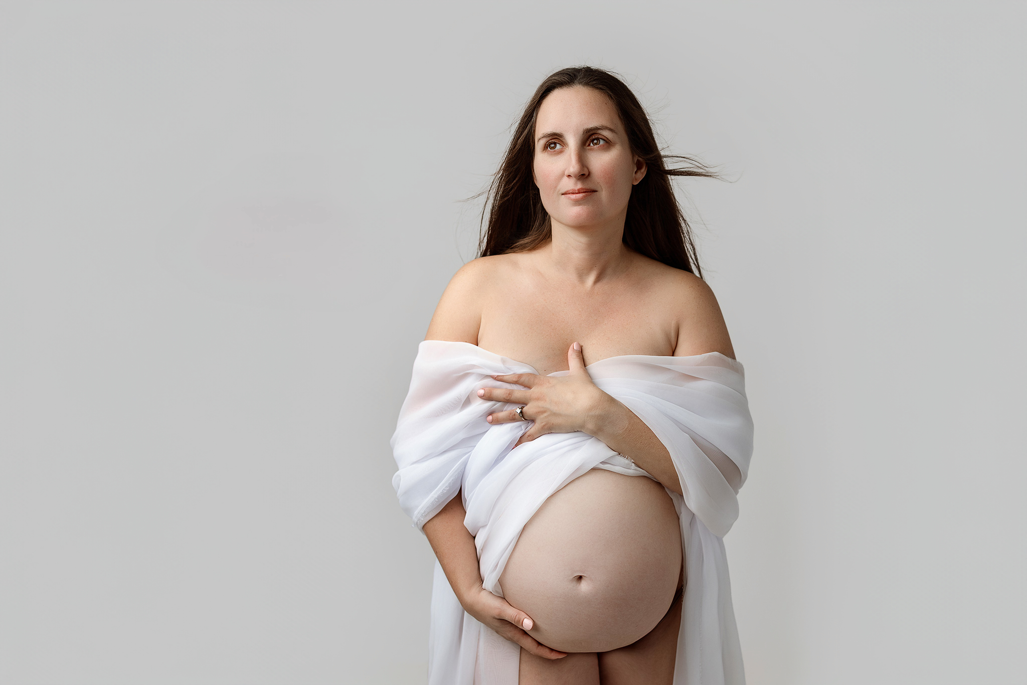 Minimal studio maternity photography of a pregnant mother standing confidently against a neutral backdrop in a Grand Rapids studio
