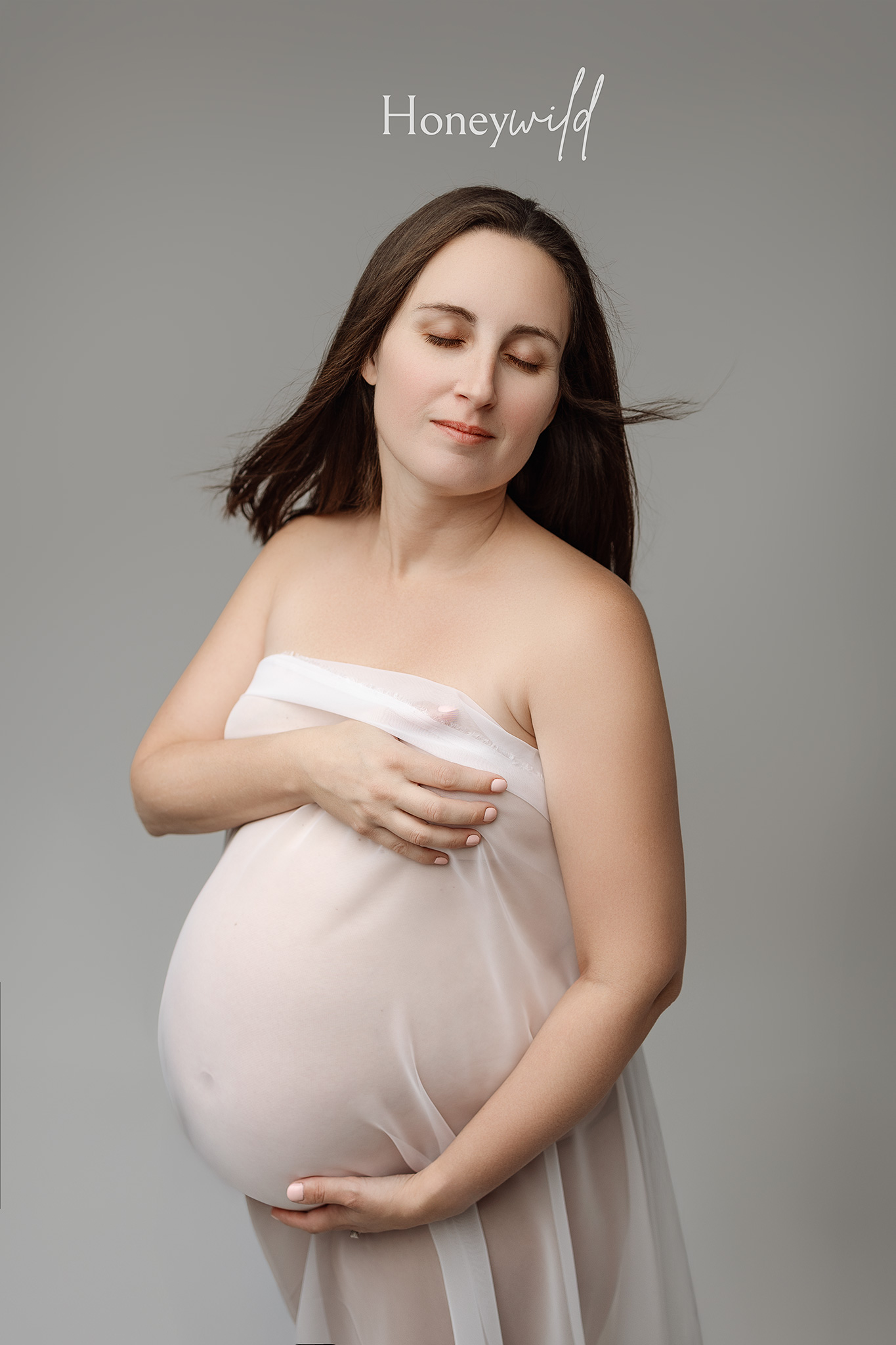 Intimate studio maternity photograph of an expecting mother with eyes closed, highlighting softness, trust, and pregnancy connectio