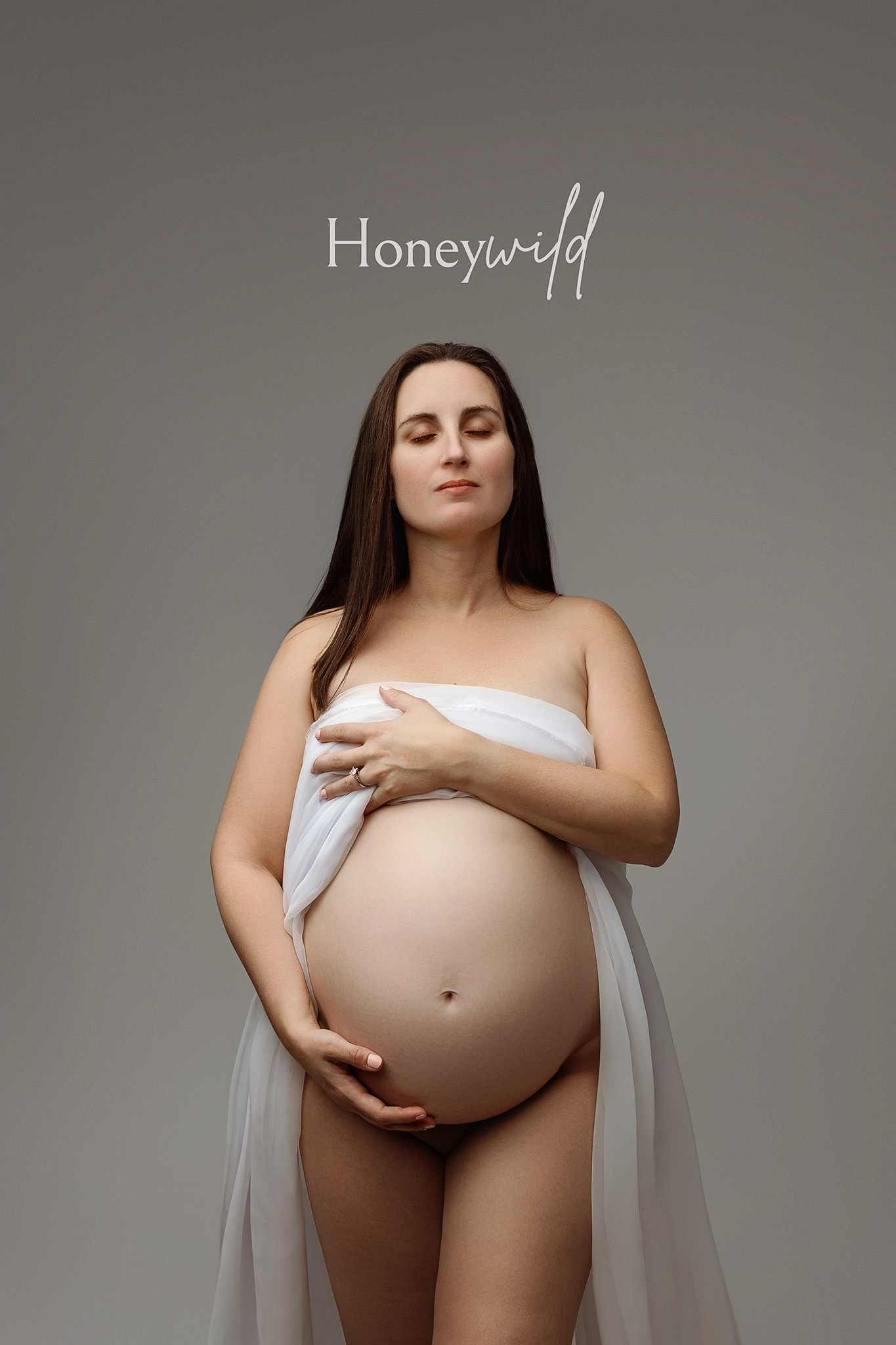 Minimal studio maternity photography of a pregnant mother standing confidently against a neutral backdrop in a Grand Rapids studio