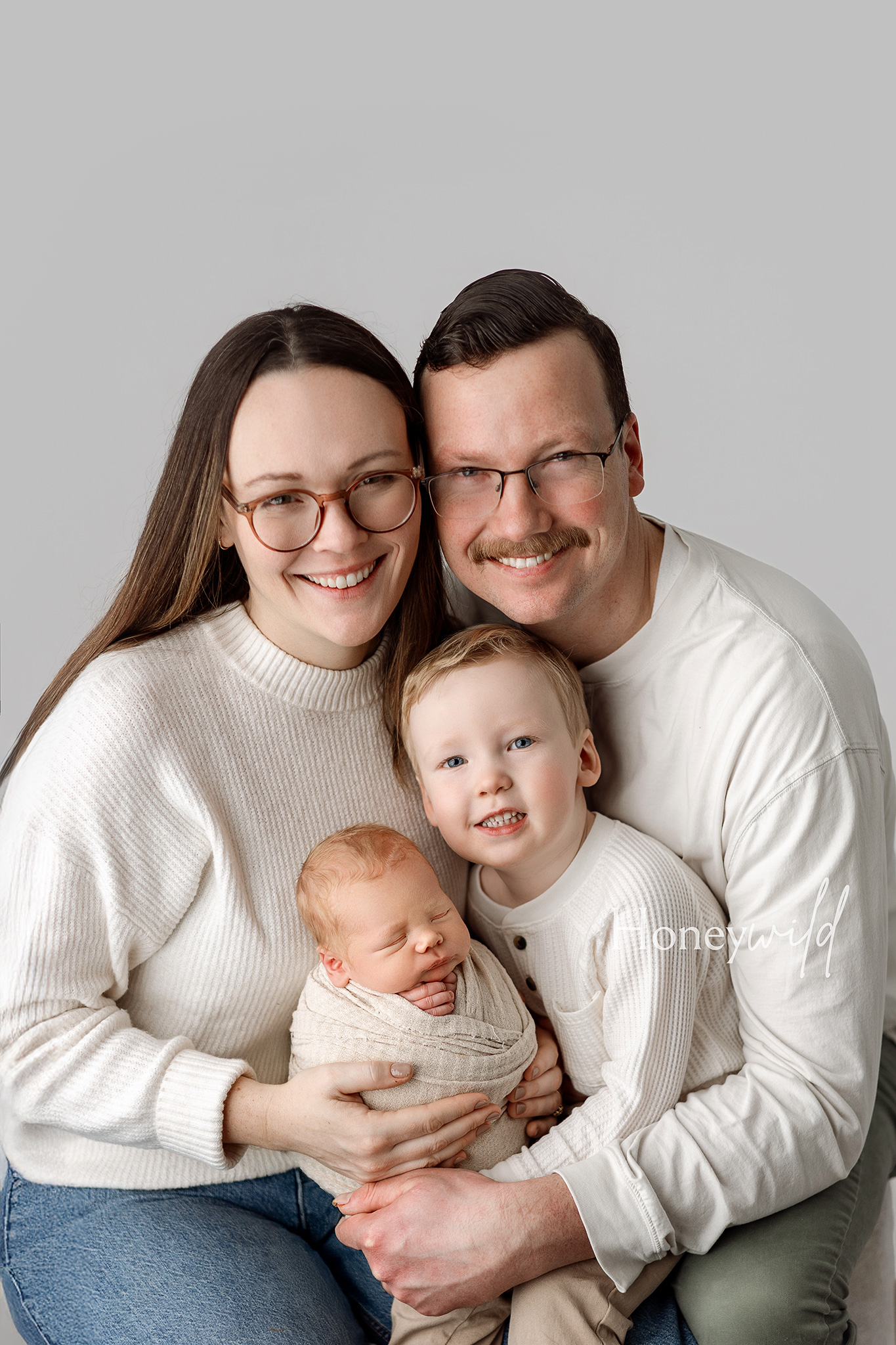 Newborn photography session in Grand Rapids featuring parents holding their baby in a calm, minimal studio environment in January 2026