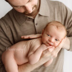 New father holding his newborn baby close during a peaceful, intentional newborn photography session