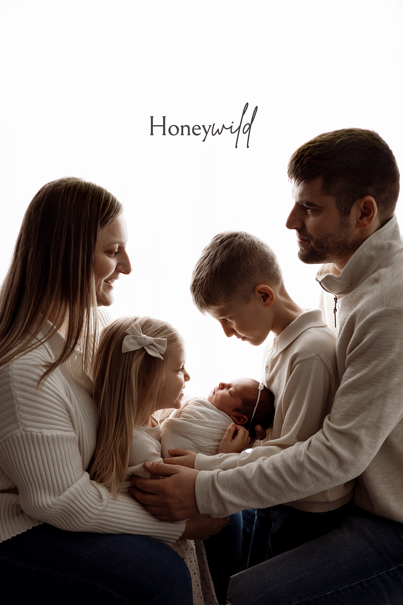 Studio newborn session with family looking at baby in soft neutral colors and backlit