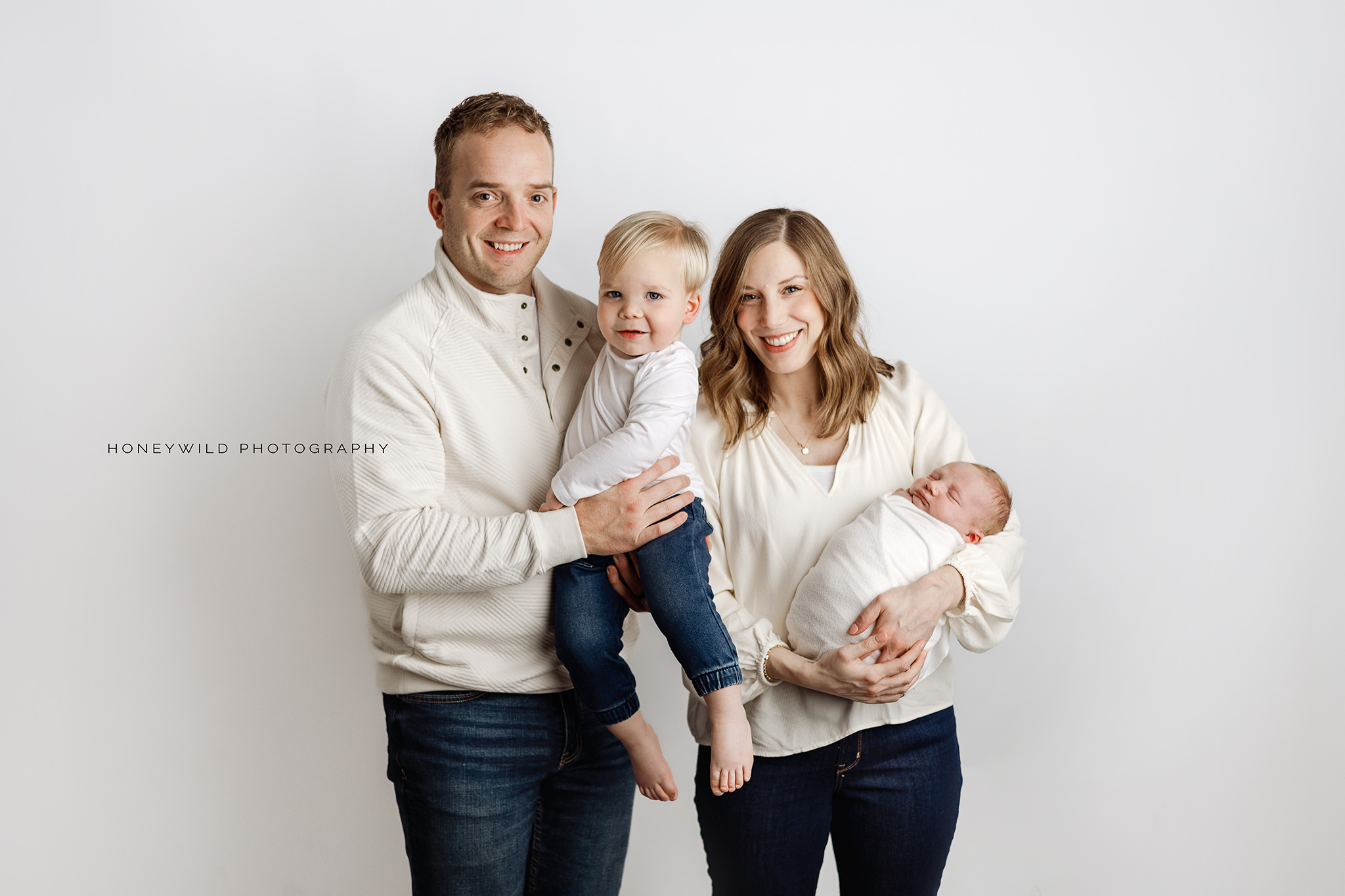 Studio newborn session in Grand Rapids featuring parents and siblings holding their newborn in soft neutral tones  in January 2025