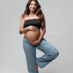 Casual maternity photography Grand Rapids, expecting mother in jeans and black top against light grey backdrop