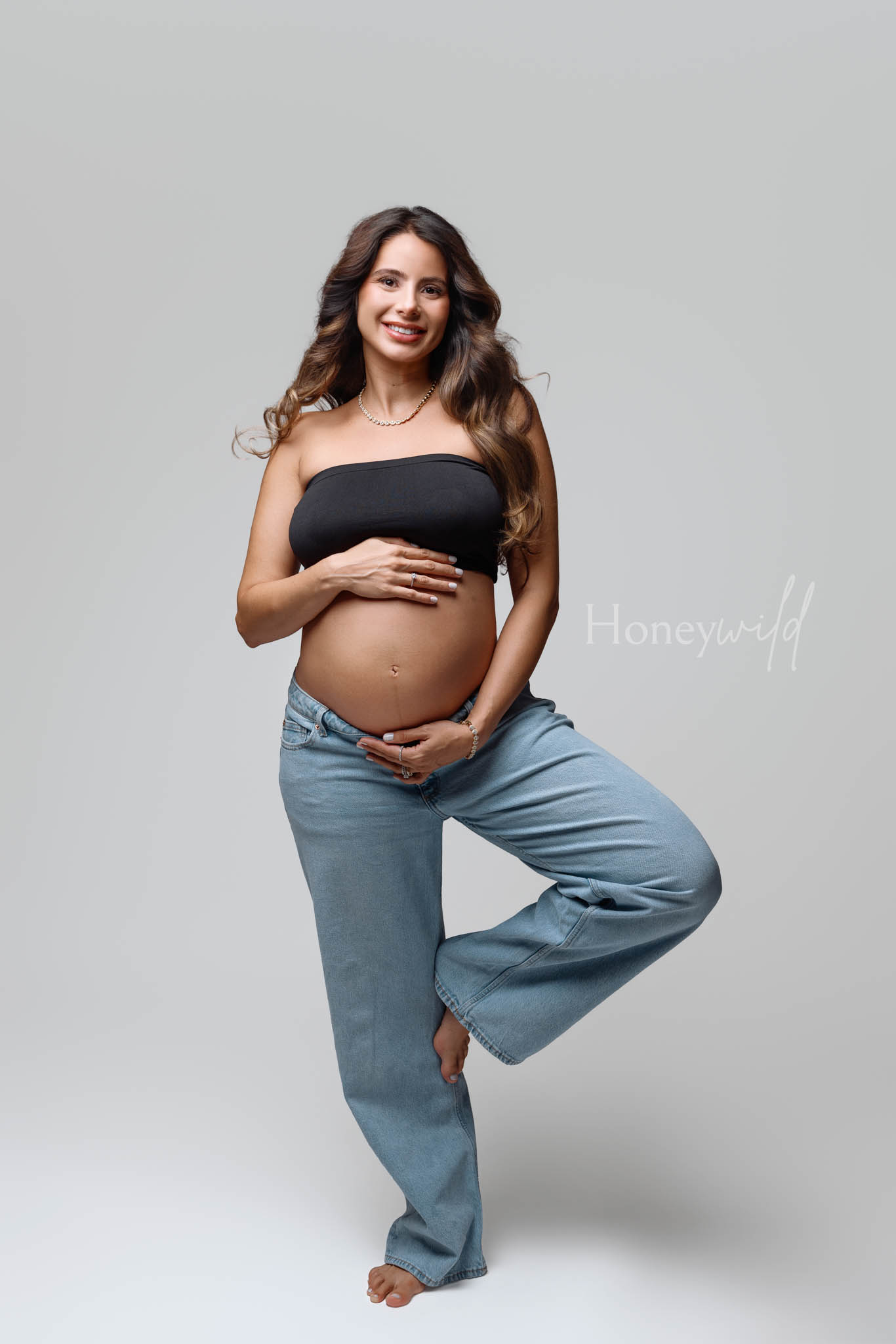 Casual maternity photography Grand Rapids, expecting mother in jeans and black top against light grey backdrop