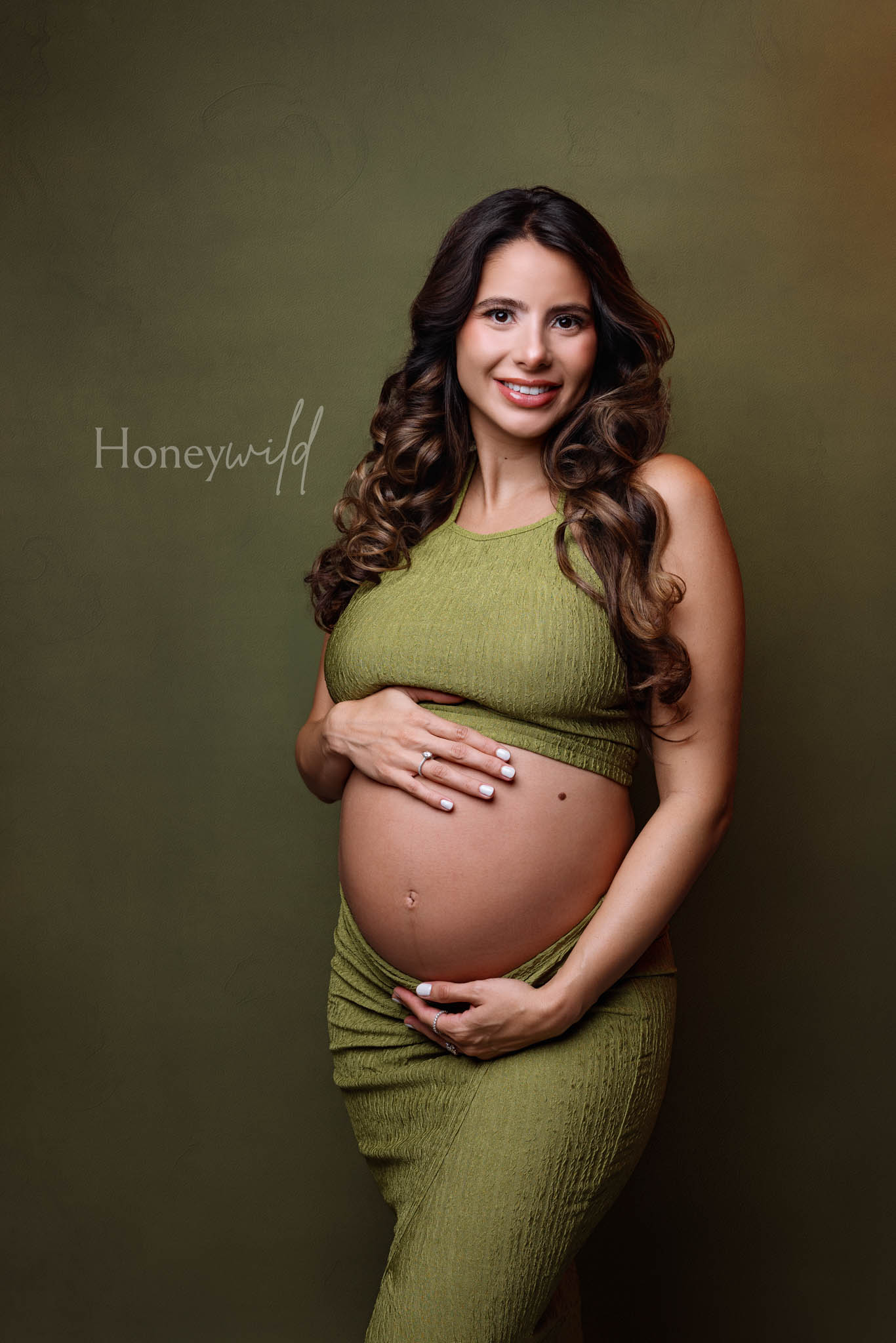 Studio maternity photography Grand Rapids, expecting mother in fitted green dress against dark backdrop