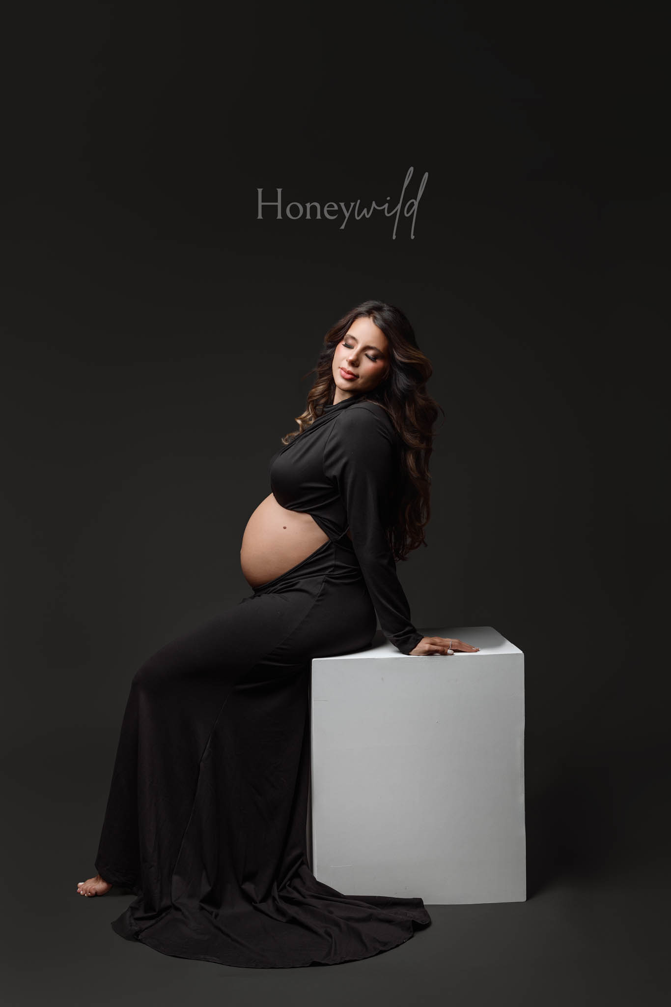 Editorial maternity photographer Grand Rapids, seated studio pose in black gown against dark backdrop