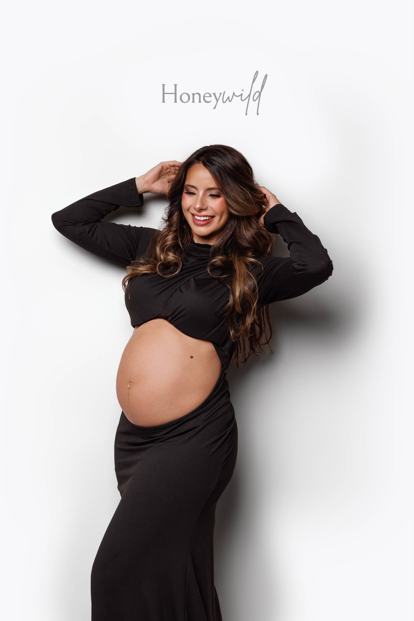 Studio maternity photographer Grand Rapids, candid smiling pose in black maternity gown against white backdrop