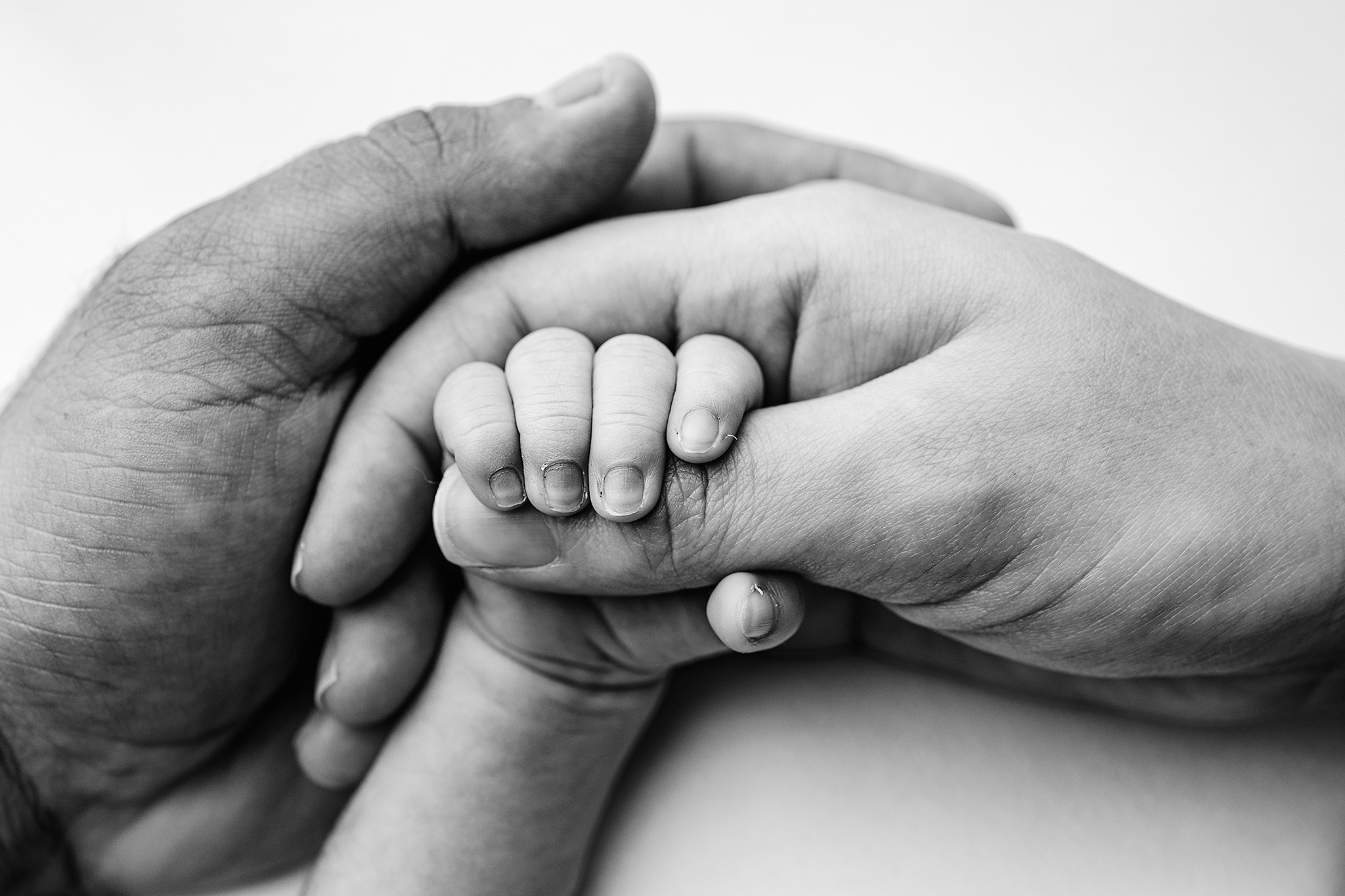 Black and white close-up of a newborn's hand gripping a parent's finger, detail shot by a Grand Rapids Newborn photographer