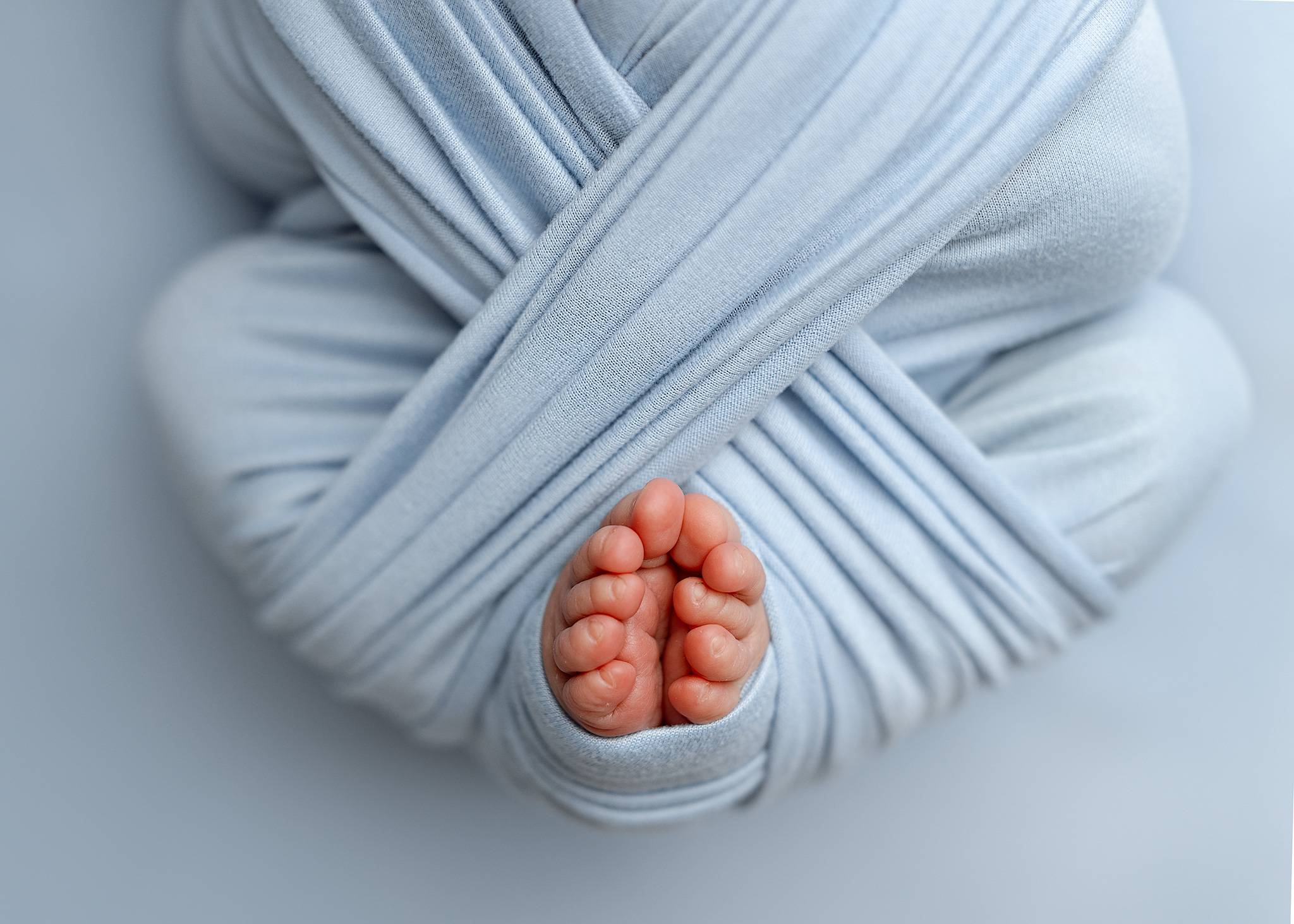 Close-up of a newborn's tiny toes peeking out from a light blue swaddle wrap during a session with a Grand Rapids newborn photographer
