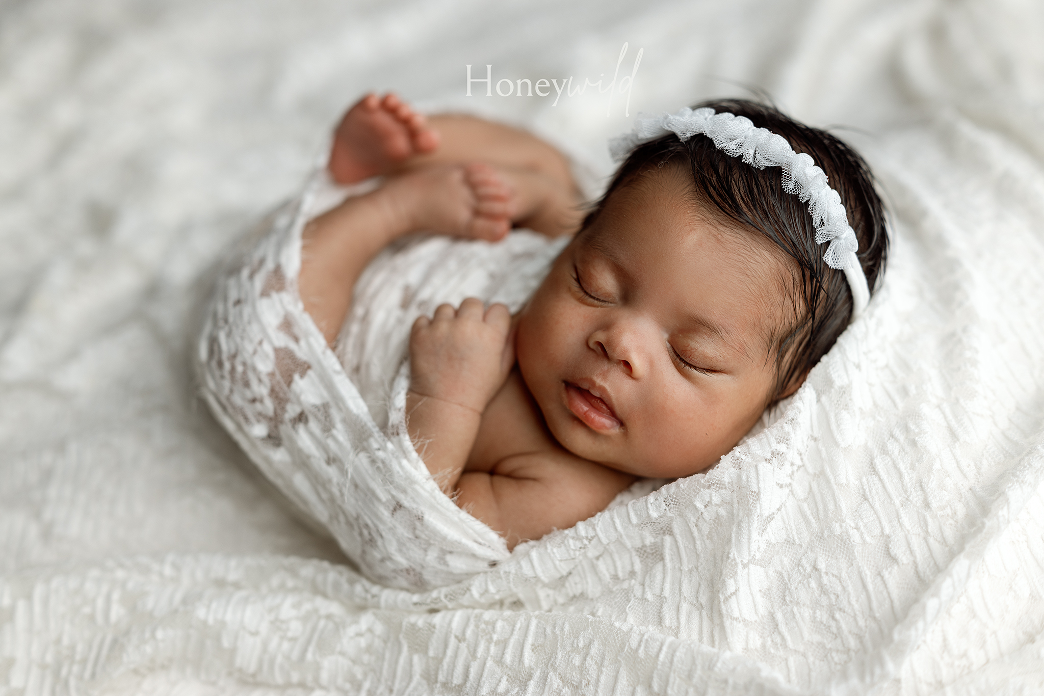 Grand Rapids newborn photographer image of a sleeping baby girl in a white lace wrap and flower headband with her feet up