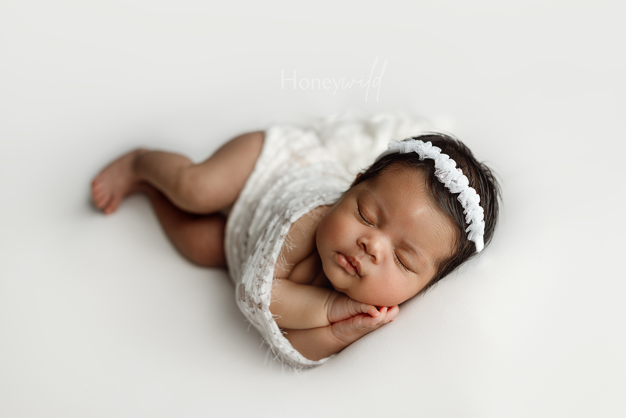 West Michigan newborn photography of a baby girl sleeping on her side in a cream lace wrap and floral headband