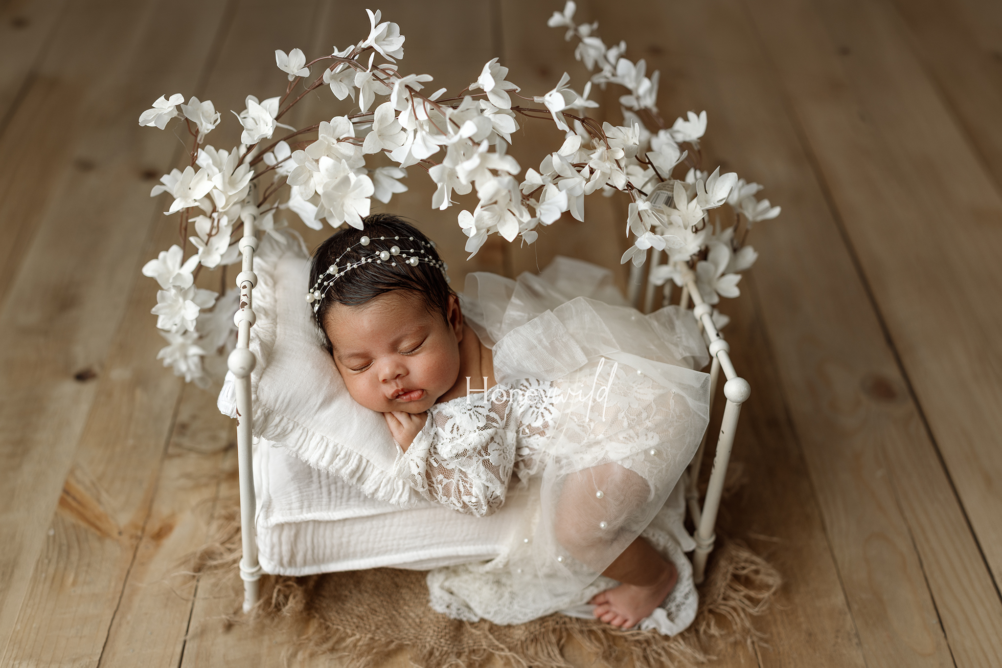 Newborn photos in Grand Rapids MI of a sleeping baby in a white bed with blossom branches and a pearl headband